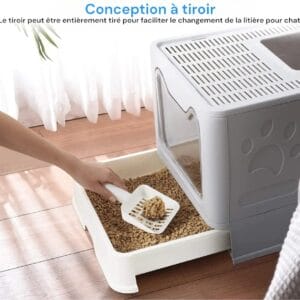 Image d'une litière pour chat avec une conception à tiroir. Une main tient une pelle pour faciliter le changement de litière. Le tiroir peut être tiré pour un nettoyage facile, et la litière est visible à l'intérieur.